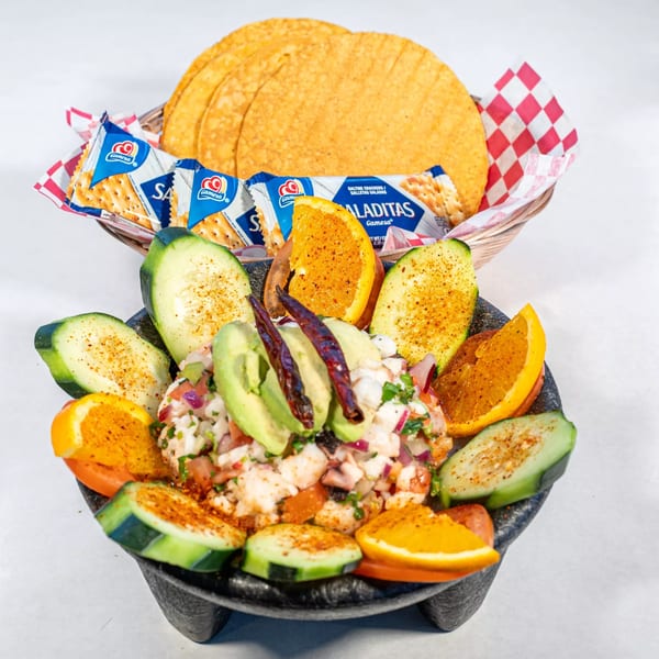 Ceviche in a molcajete, garnished with avocado, cucumber, orange slices, and dried chilies, with tortillas and crackers.