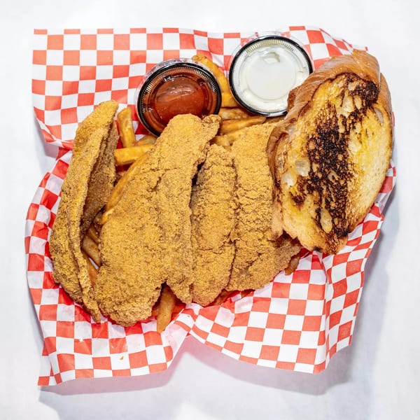Fried catfish fillets, french fries, garlic bread, ketchup, and tartar sauce in a red checkered basket.