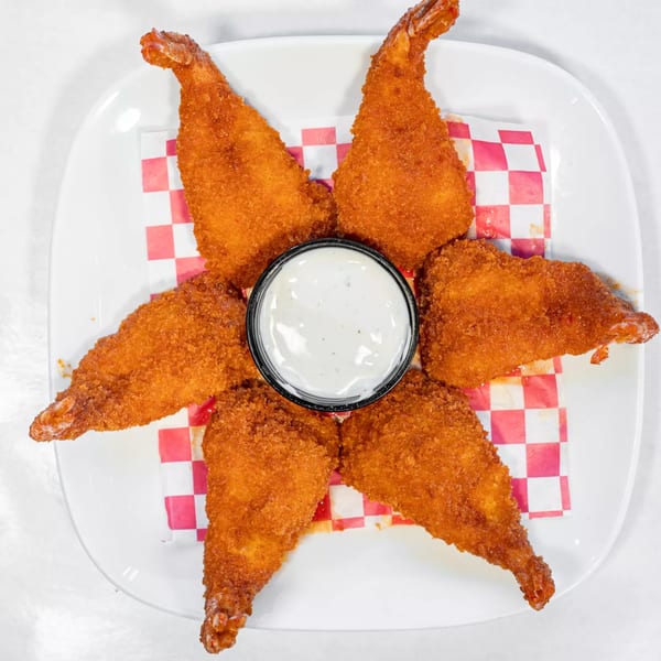 Six crispy fried shrimp arranged around a small cup of white dipping sauce on a white plate.