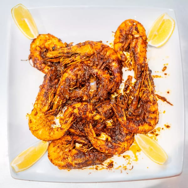 Cajun-spiced shrimp with lemon wedges on a white plate at Cajun Crab & Shrimp Bar & Grill.
