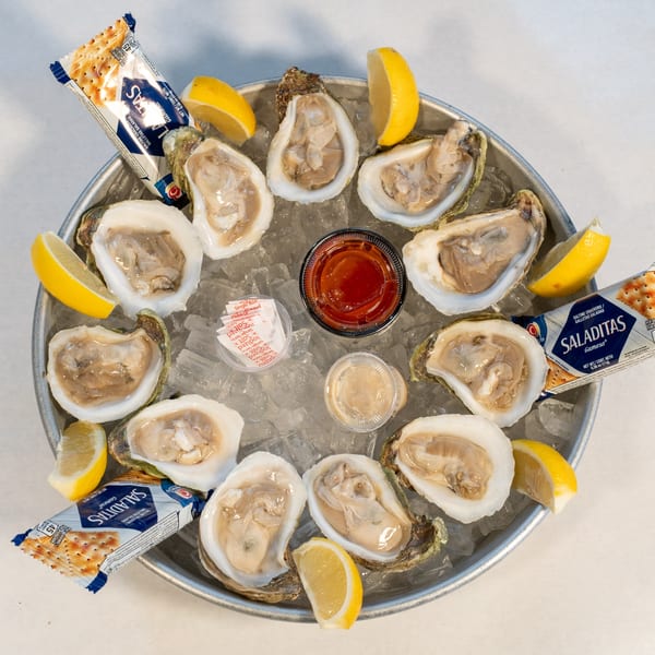 A dozen fresh oysters on the half shell, served on ice with lemon wedges, crackers, and sauces.