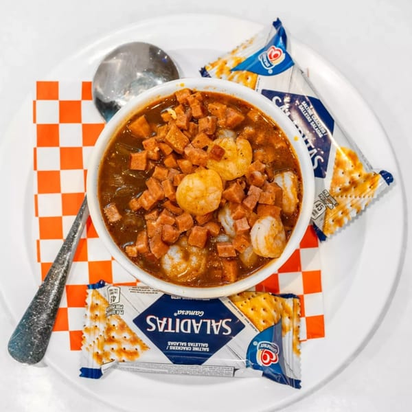 Cajun shrimp and sausage gumbo in a white bowl with crackers and a spoon on a white plate.