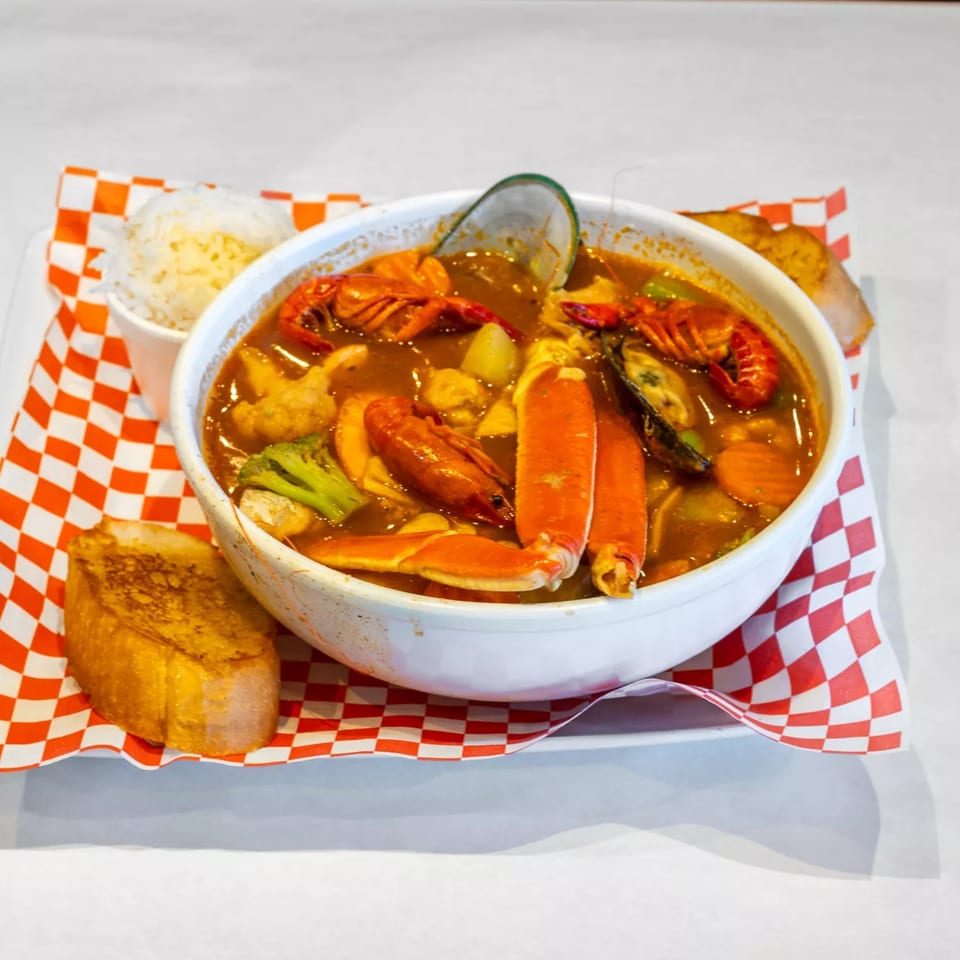Cajun seafood boil with crab legs, crawfish, mussels, and vegetables, served with rice and garlic bread.