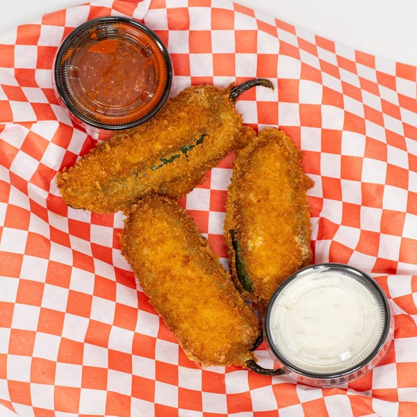 Three golden-brown fried jalapeño poppers with red and white checkered paper, served with two dipping sauces.
