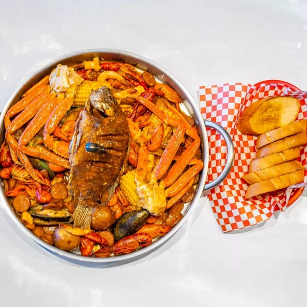 Cajun seafood boil with whole fish, crab legs, crawfish, corn, and potatoes, served with sliced bread.