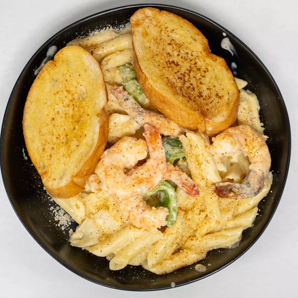 Cajun Shrimp Pasta with penne, creamy sauce, green peppers, and two slices of garlic bread.