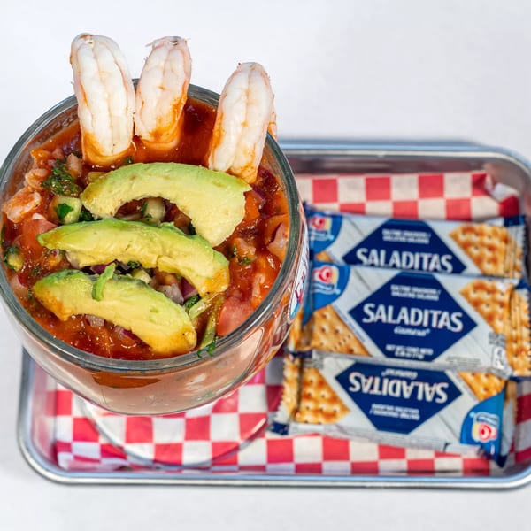 Shrimp cocktail with avocado slices and three shrimp, served with Saliditas crackers on a tray.
