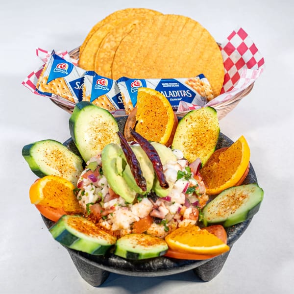 Ceviche in a molcajete with cucumber, orange slices, avocado, dried chilies, and a side of tostadas and crackers.
