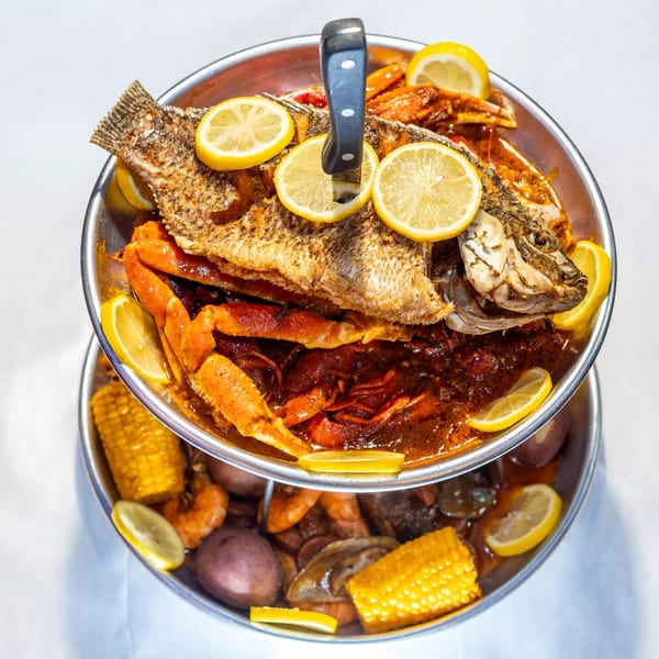 A two-tiered seafood boil with a whole fried fish, crab, crawfish, corn, and potatoes.