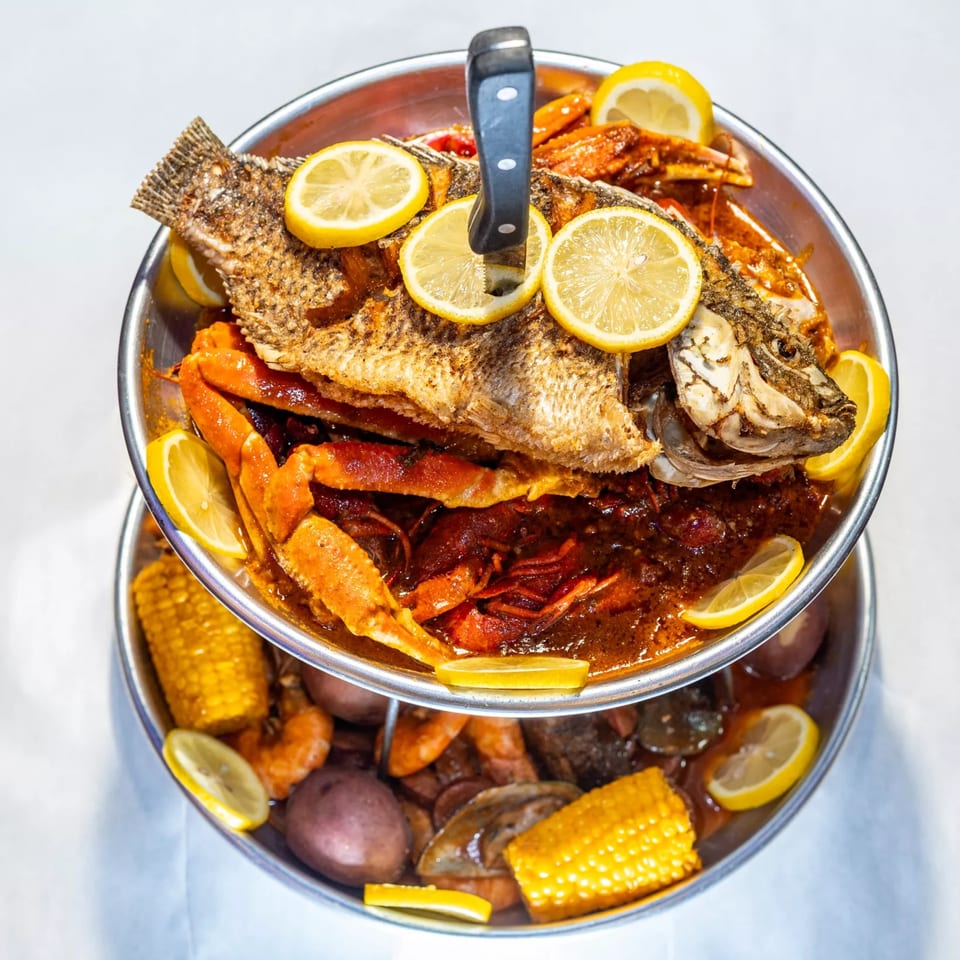 A two-tiered seafood boil with a whole fried fish, crab, crawfish, corn, and potatoes.
