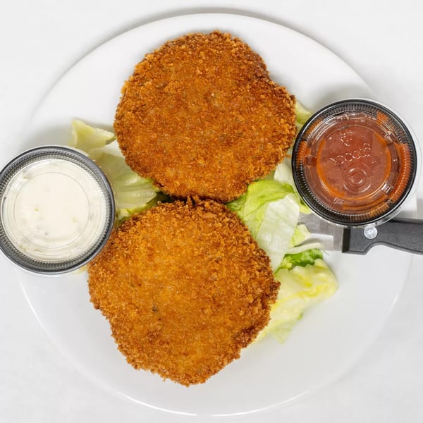 Two crispy fried crab cakes on lettuce with tartar sauce and cocktail sauce on a white plate.
