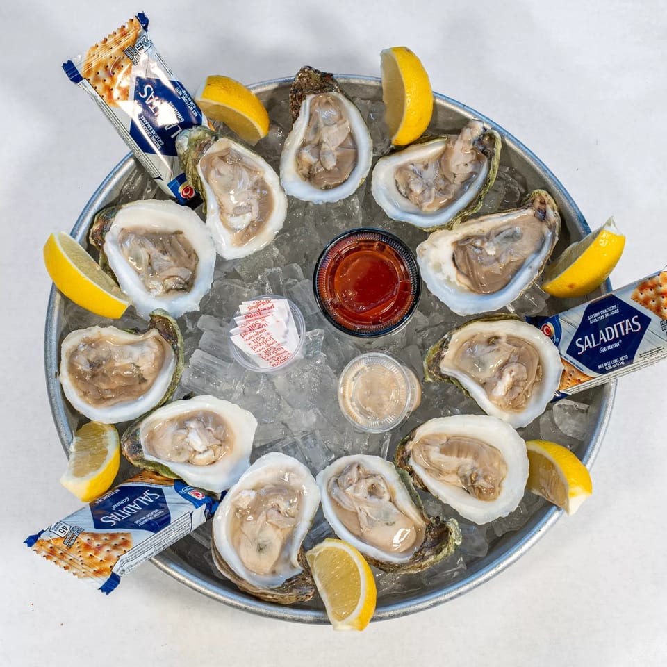 A dozen fresh oysters on the half shell, served on ice with lemon wedges, cocktail sauce, and crackers.